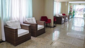 Un vestíbulo de hotel con sillas de mimbre, una silla roja y una zona de recepción.