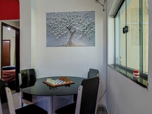 Ein Essbereich mit einem runden Tisch, Stühlen und einem Schachbrett. An der Wand hängt ein Baumgemälde.