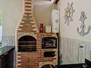 Eine Außenküche aus Backsteinen mit Pizzaofen, einem roten Gasflasche und dekorativer Wandgestaltung.