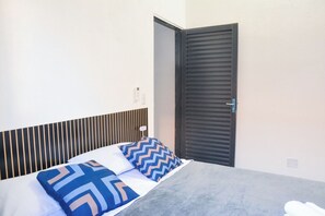 Ein Hotelzimmer mit einem Bett, einem grauen Sofa, einem gestreiften Kopfteil und einer geschlossenen Tür.