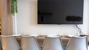 Un comedor con cuatro sillas grises, una mesa de madera y un televisor de pantalla plana montado en la pared.