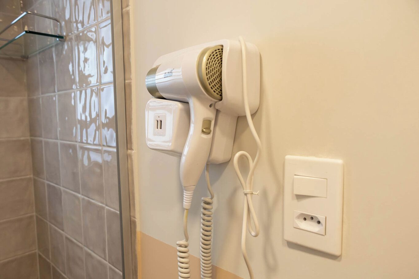 A hair dryer mounted on a wall with a power outlet and a switch.