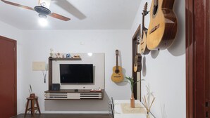 Un salon avec un téléviseur, des guitares, une plante et un jeu de puzzle sur le sol.