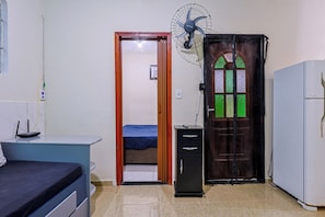 Une chambre comprenant un lit, un bureau, un ventilateur, une armoire et une porte ornée de vitraux.