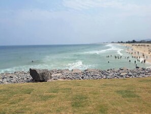 A beach with a rocky shoreline, a grassy foreground, and a distant view of the ocean. - House with Wi-Fi and Garage 5 min from Downtown (Maricá)