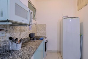 A compact kitchen with a granite countertop, a microwave, a sink, and a refrigerator. - Loft c/ Ar e Wi-Fi a 100m da Praia de Copacabana (Rio de Janeiro)