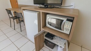 Una kitchenette compacta con refrigerador, microondas y un pequeño armario con vasos.