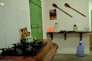 Eine Küche mit einem Gasherd, Holzkochinstrumenten, einer grünen Tür und einem an der Wand hängenden Bild.