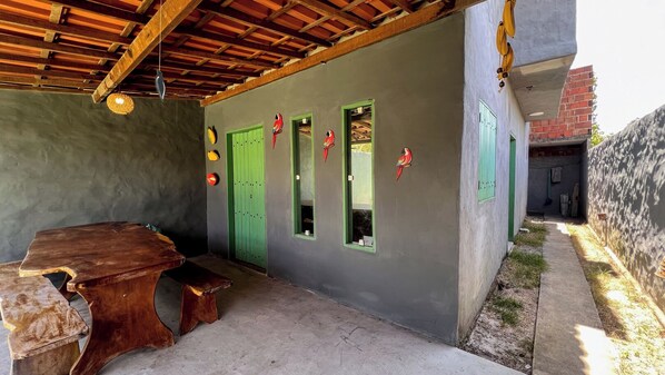 A covered outdoor area with a wooden table and benches, a green door, and a window with a view of a brick building. - Casa Brisa das Águas: Pool and BBQ (Tatuamunha)