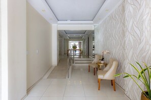 Eine Hotelhalle mit modernem Design, mit Marmorboden, einer Rezeption und einer Sitzecke mit Stühlen und einem kleinen Tisch.