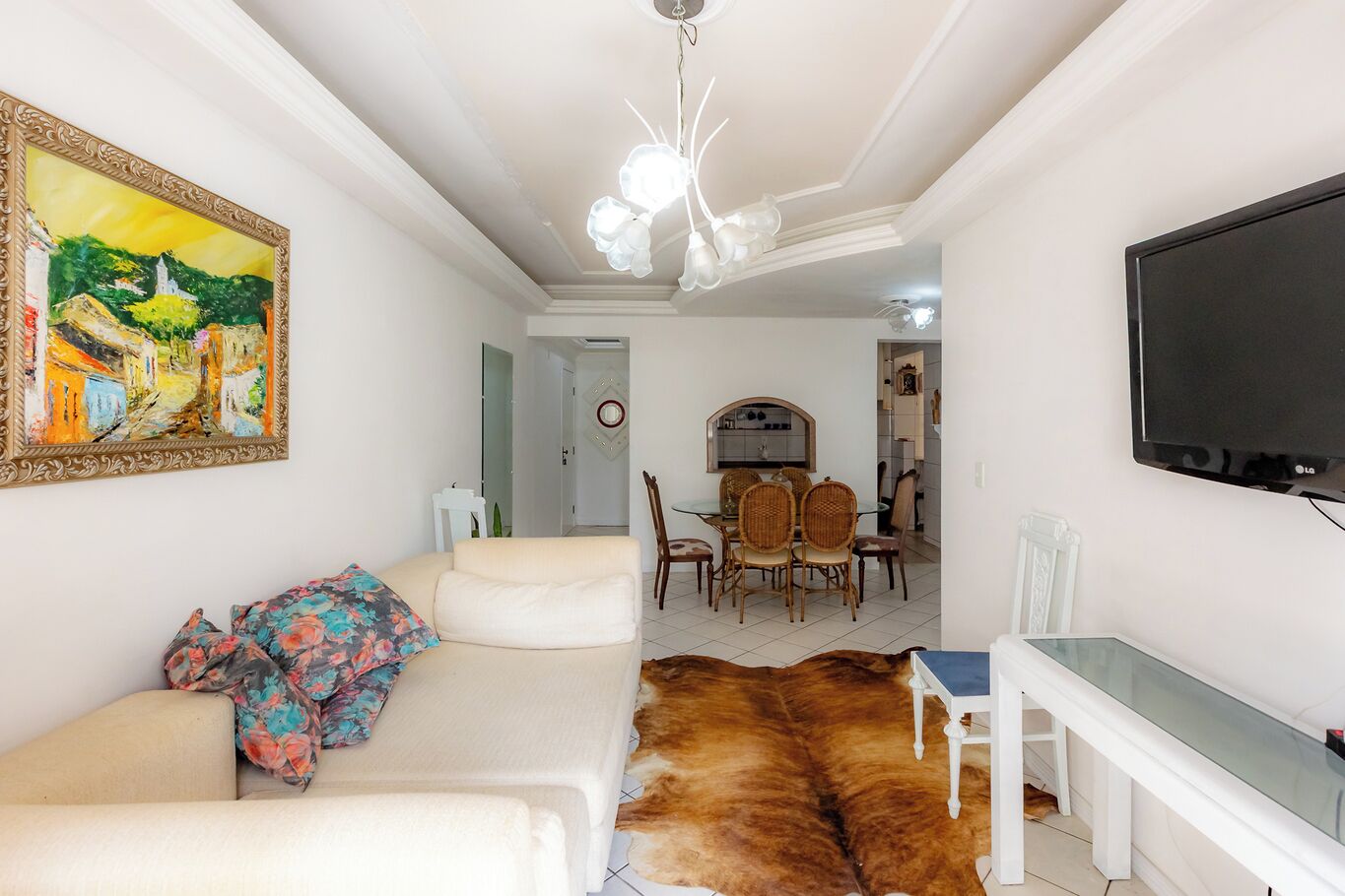 Una sala de estar con un sofá, una mesa de comedor con sillas, un televisor y un cuadro en la pared.