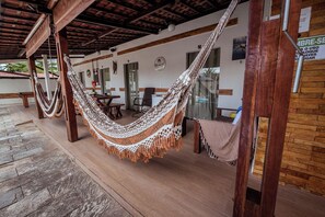 Eine Hängematte unter einer Holzw pergola in einem überdachten Außenbereich mit Steinboden und Backsteinwand.