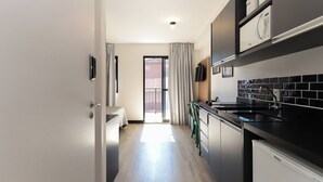 Eine moderne Küche mit schwarzen Arbeitsflächen, einem Spülbecken und einem eingebauten Backofen. Es gibt eine Essecke mit Tisch und Stühlen sowie eine Glastür, die auf einen Balkon führt.