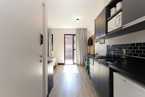 Eine moderne Küche mit schwarzen Arbeitsflächen, einem Spülbecken und einem eingebauten Backofen. Es gibt eine Essecke mit Tisch und Stühlen sowie eine Glastür, die auf einen Balkon führt.
