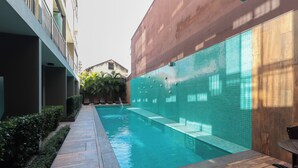 Ein Schwimmbecken mit gefliesten Wänden, einer Holzdielen-Terrasse und einem kleinen Tisch.