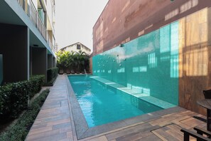 Ein Schwimmbecken mit gefliesten Wänden, einer Holzdielen-Terrasse und einem kleinen Tisch.