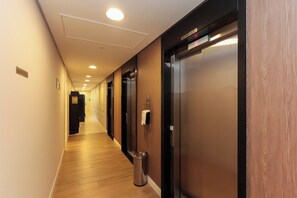 Ein Hotelgang mit Holzboden, einem Mülleimer und zwei Aufzügen.
