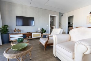 A modern living room with a sofa, armchairs, a TV, and a dining area with a table and chairs. - Cobertura Duplex com piscina a 200m da Praia (Guarujá)