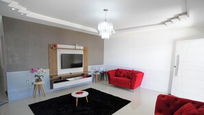 Ein modernes Wohnzimmer mit Fernseher, einem roten Sofa, einem schwarzen Teppich und einem kleinen Beistelltisch mit Blumen in einer Vase.