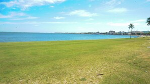 Eine grüne Fläche mit Blick auf das Meer und eine in der Ferne liegende Küstenlinie mit Gebäuden.