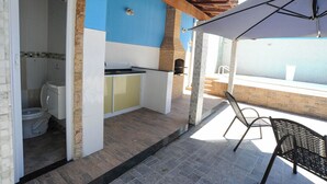 Ein überdachter Außenbereich mit Grill, einer Sitzecke mit Tisch und Stühlen sowie Blick aufs Meer.