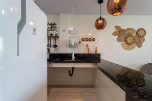 Eine moderne Küche mit weißen Schränken, einer schwarzen Arbeitsplatte und einem Spülbecken. Es befinden sich Küchenutensilien zum Aufhängen und ein dekoratives Wandbild dort.