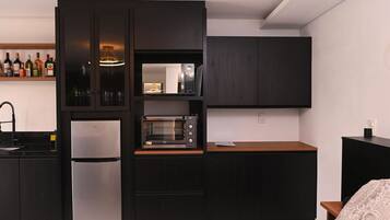 Et moderne køkken med indbygget ovn, køleskab og mikrobølgeovn. En hylde med flasker og glas, samt en træbordplade.