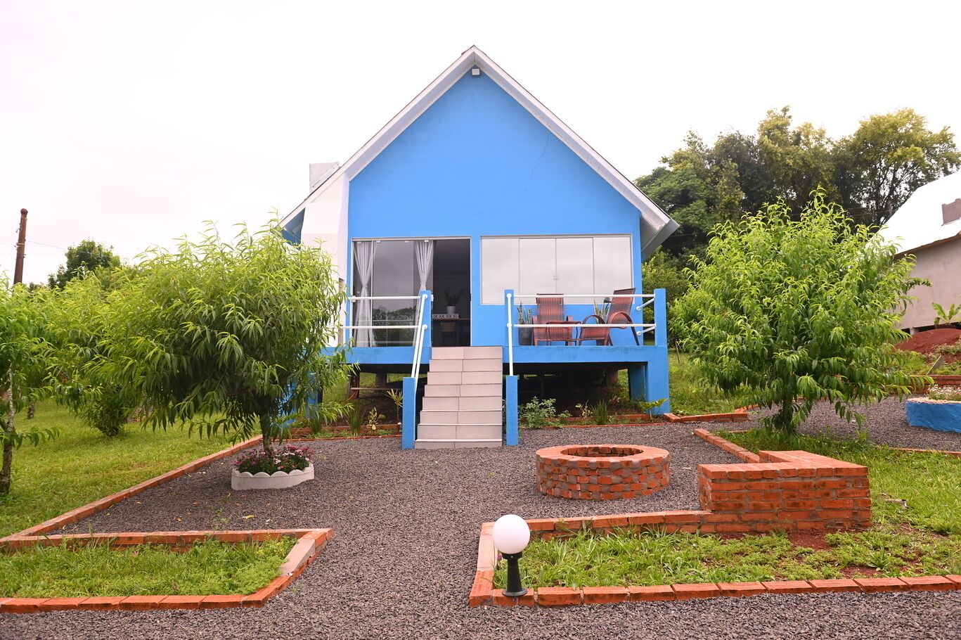 Une maison bleue avec un balcon, un petit jardin et un foyer en briques.