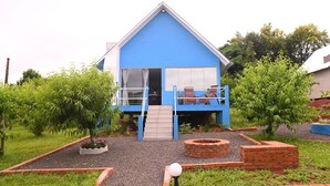 A blue house with a balcony, a small garden, and a brick fire pit. - Cabana Horizonte Azul com Hidro e Churrasqueira (Santa Rosa de Lima)
