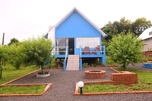 Ein blaues Haus mit Balkon, kleinem Garten und einem Feuerkorb aus Ziegelsteinen.