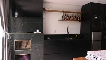 A modern kitchen with black cabinets, a marble backsplash, a built-in TV, a wine rack, and a wooden shelf.