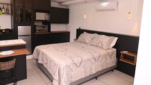 A compact hotel room with a bed, a small desk, a kitchenette, and a bedside table. - Cabana Horizonte Azul com Hidro e Churrasqueira (Santa Rosa de Lima)