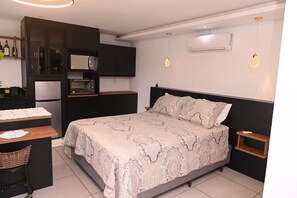Ein kleines Hotelzimmer mit Bett, Schreibtisch, Küchenzeile und Nachttisch.