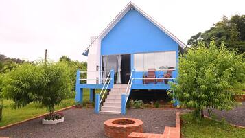 A blue house with a balcony, a staircase, and a brick fire pit.