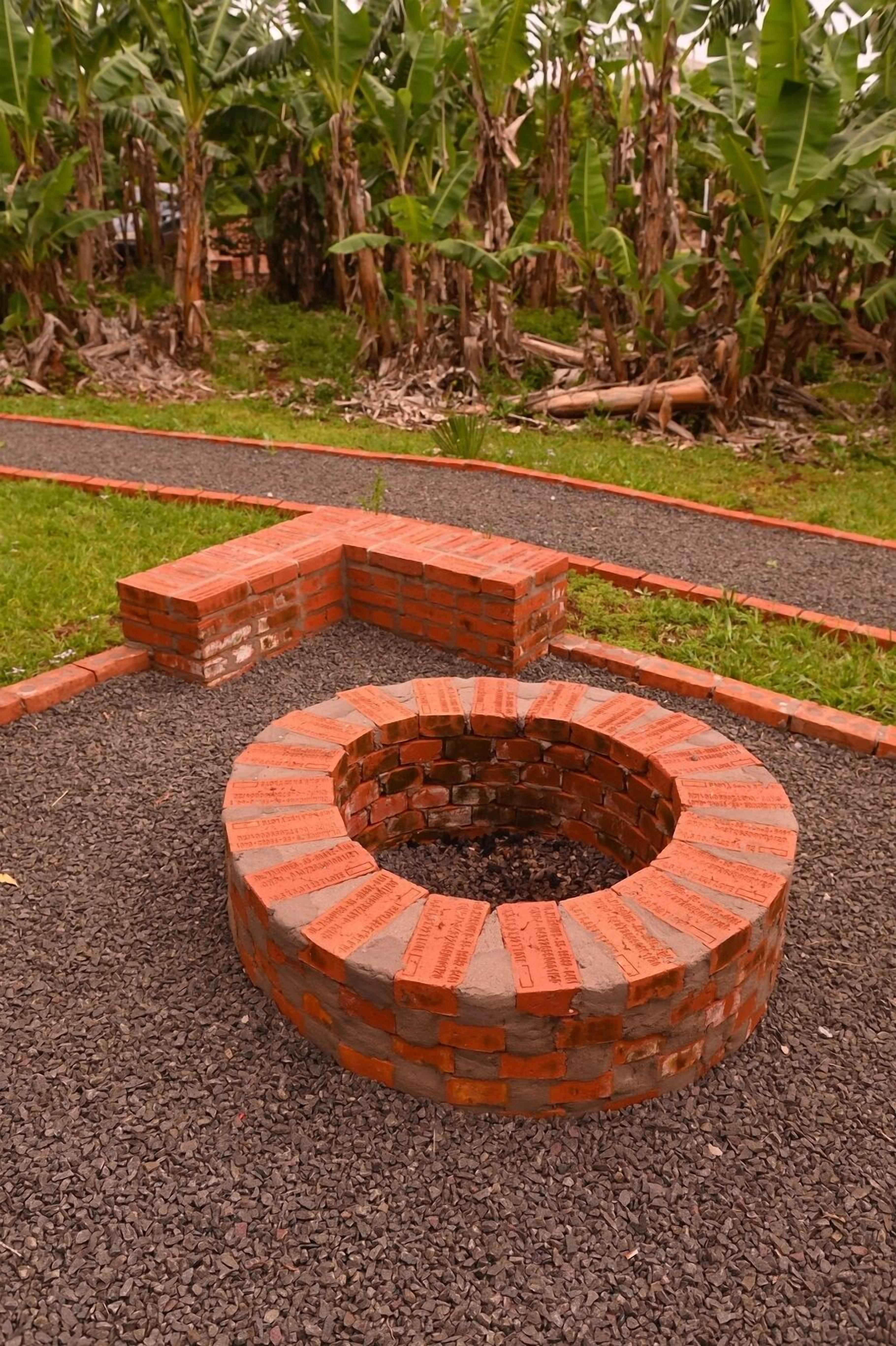 A circular brick fire pit with a brick border, surrounded by gravel and a brick pathway.