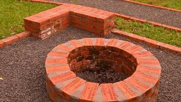 A circular brick fire pit with a brick border, surrounded by gravel and a brick pathway.