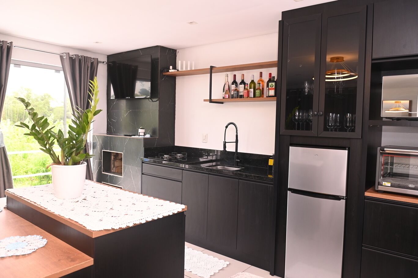 A modern kitchen with black cabinets, a stainless steel refrigerator, a built-in oven, and a wine shelf.