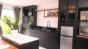 A modern kitchen with black cabinets, a stainless steel refrigerator, a built-in oven, and a wine shelf.