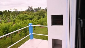 A balcony with a white railing, a blue post, and a view of a lush garden. - Cabana Horizonte Azul com Hidro e Churrasqueira (Santa Rosa de Lima)