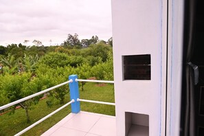 Ein Balkon mit weißer Reling, einer blauen Säule und Blick auf einen üppigen Garten.