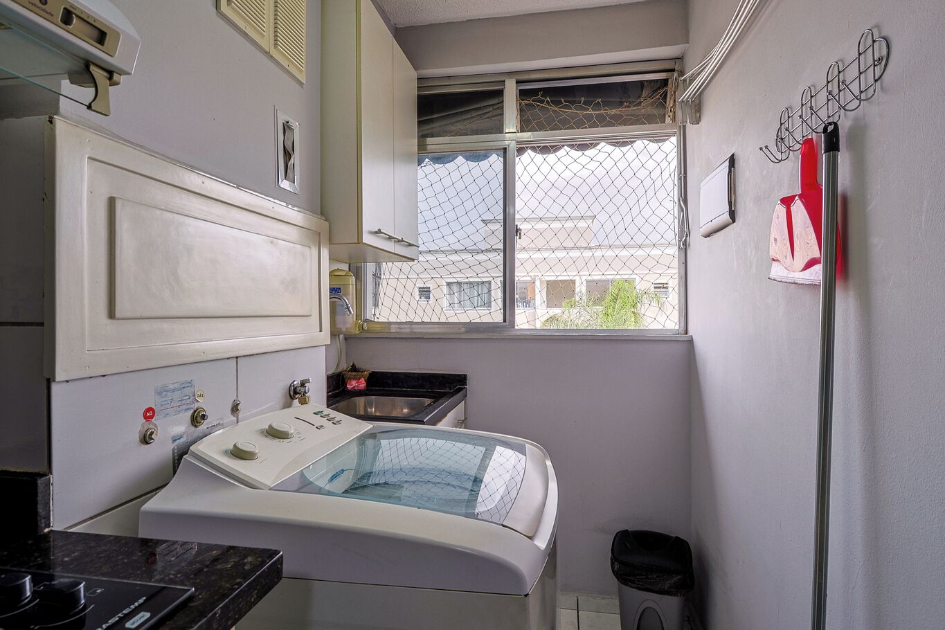 A compact laundry room with a washing machine, a sink, and a window with a view of buildings outside.