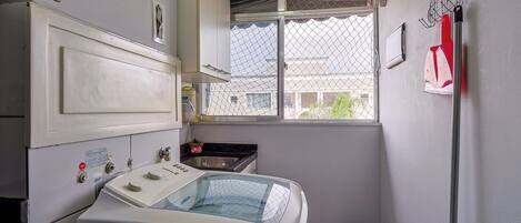 A compact laundry room with a washing machine, a sink, and a window with a view of buildings outside.