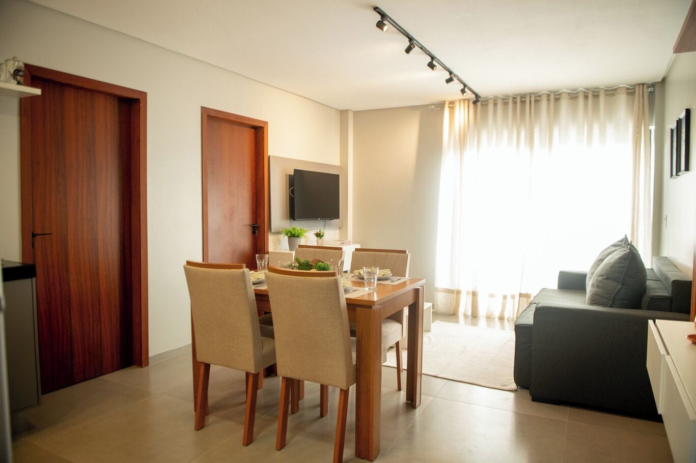 A modern living room with a dining area, a sofa, and a TV mounted on the wall.