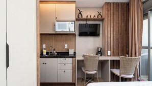 Eine kleine Küche mit Mikrowelle, Spüle und Holzschränken. Zwei Korbstühle und ein an der Wand befestigter Fernseher sind vorhanden.