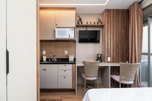 Eine kleine Küche mit Mikrowelle, Spüle und einem Flachbildfernseher. Zwei Korbstühle und ein Bett befinden sich im Raum.