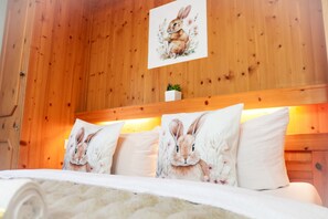 Ein Zimmer mit Holzwänden und einem Bett mit weißer Bettwäsche und Kopfkissen mit Hasenmotiven.