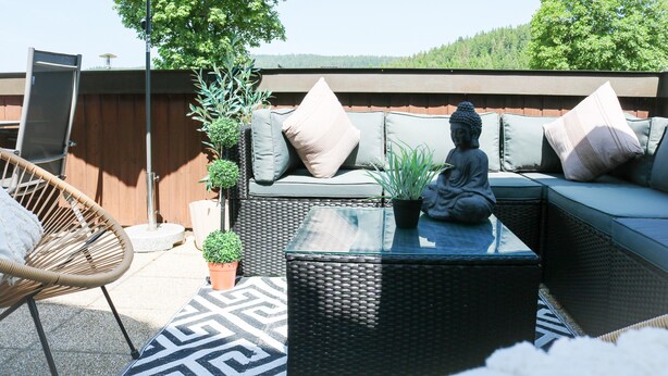 Ein Sitzbereich im Freien mit Korbmöbeln, Kissen und einer Buddha-Statue.