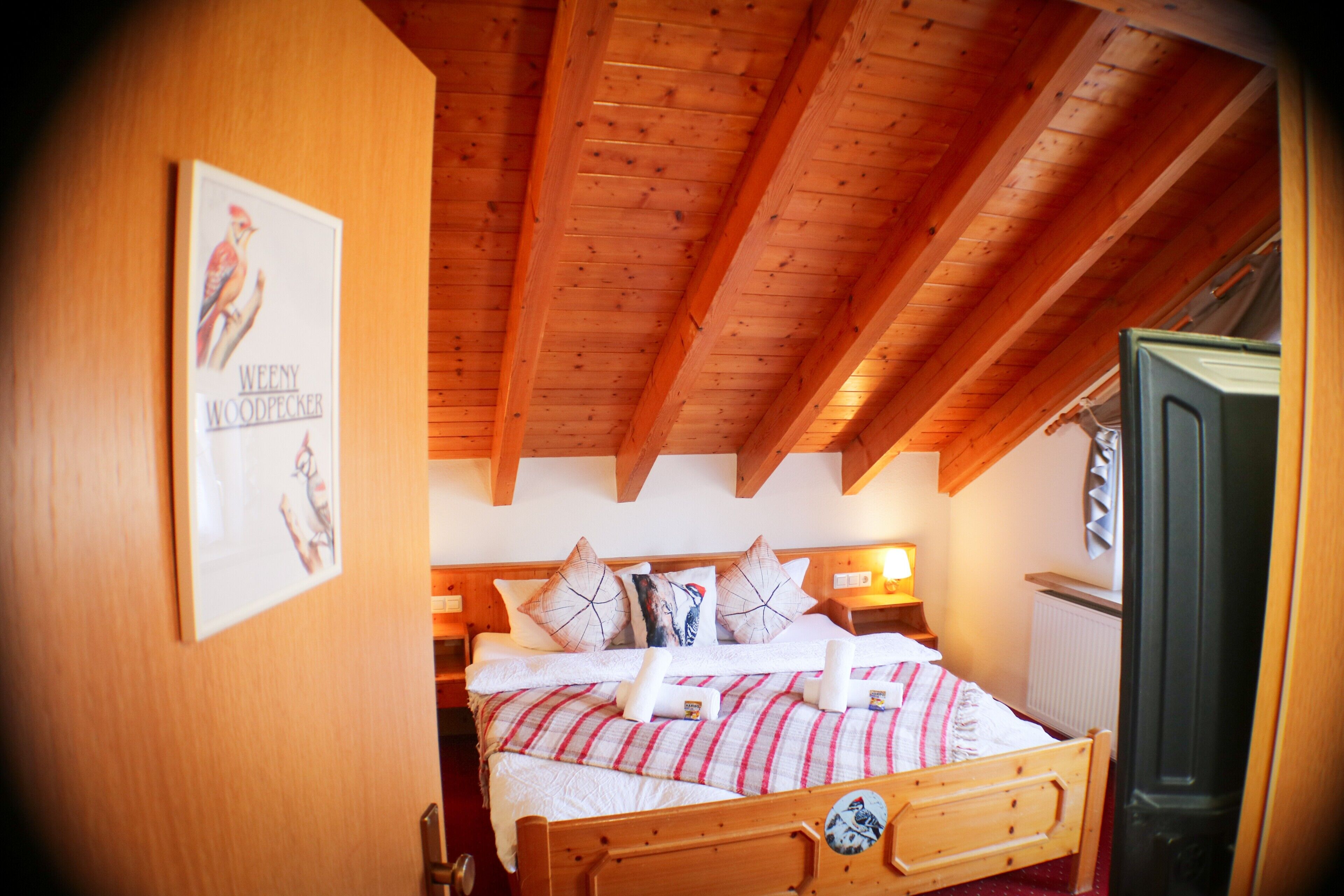 Ein schlicht eingerichtetes Schlafzimmer mit Holzbett, Kissen und einem Poster an der Wand.