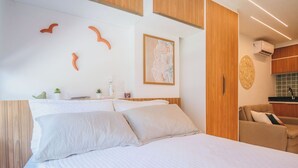 Un dormitorio con cama, cabecera de madera, una mesita con una planta y una obra de arte en la pared.