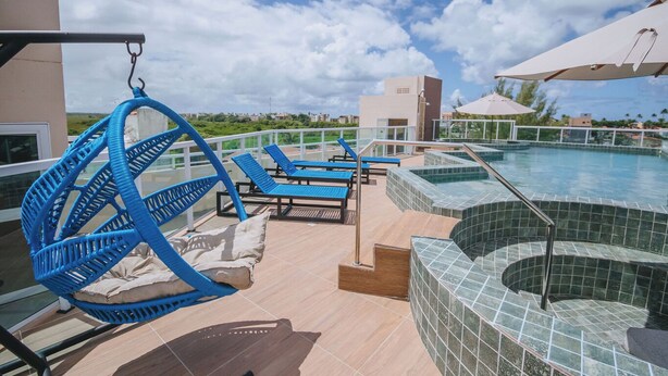 Un área de piscina en la azotea con sillones, un jacuzzi y una silla colgante.